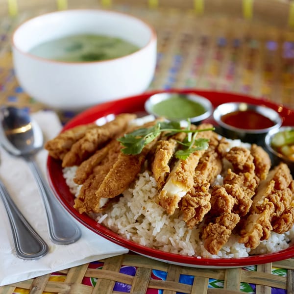 Crispy fried chicken over white rice with dipping sauces, a side of soup, and cutlery.