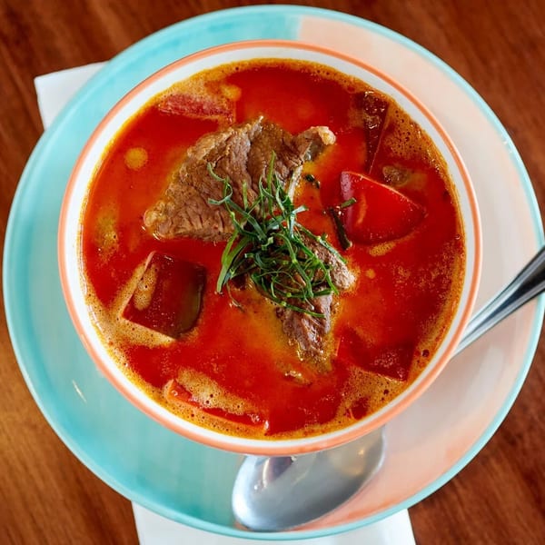 Red curry with beef, bell peppers, and herbs in a bowl on a light blue plate.