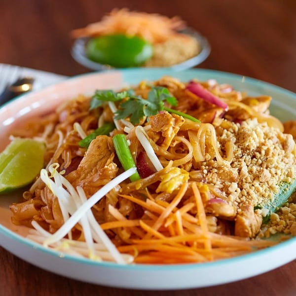 Chicken Pad Thai with lime, bean sprouts, carrots, and crushed peanuts on a colorful plate.
