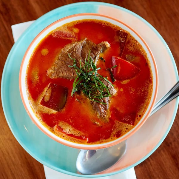 Red curry with beef, red peppers, and green herbs in a bowl with a spoon.