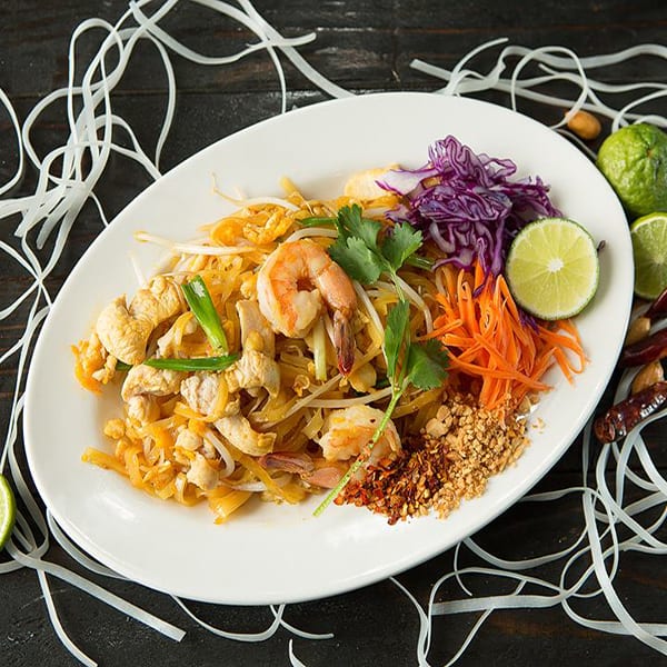 Pad Thai with chicken and shrimp, garnished with lime, carrots, cabbage, and peanuts.